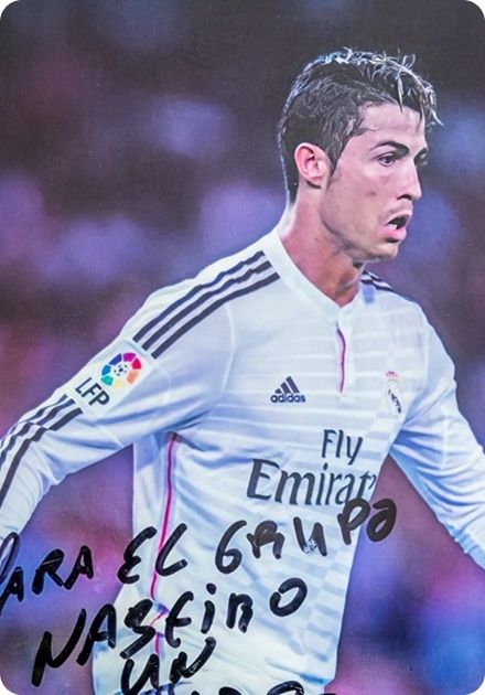 Jogador de futebol em campo, visto de perfil, a usar um equipamento branco de manga comprida com riscas escuras nos ombros e o logótipo da liga espanhola na manga esquerda; o fundo está desfocado em tons roxos e rosados, e na parte inferior da imagem vê-se uma dedicatória escrita à mão com marcador preto sobre a fotografia.